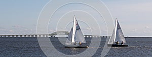 Two small sailboats competing in a winter regatta sailing north with the Great South Bay bridge in the background