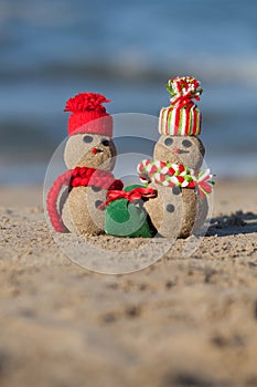 Two small sandy snowmen at tropical beach.