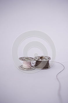 Two small spools of sewing thread of various colors isolated on a white background and also with a small sewing needle stuck in th