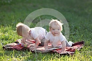 Two small twin children play on a blanket