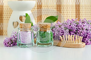 Two small vintage glass bottles with purple and green bath salts foot soak, wooden hair brush and lilac flowers. Copy space