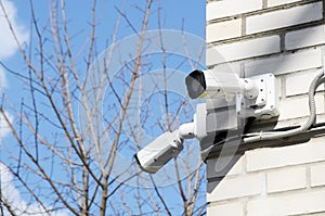 Two small white CCTV cameras on the corner of the facade of a multi-storey brick building against a blue sky