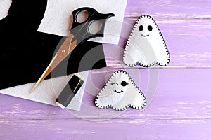 Two small white ghosts crafts, felt sheets, scissors, thread, needle on lilac wooden background. Hand Halloween decor idea