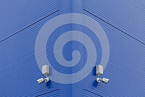 Two small white security cameras on blue steel building corner