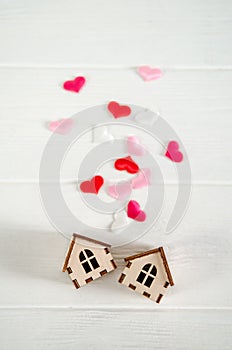 Two small wooden houses on white background, pink hearts between them, concept of family happiness, buying a house