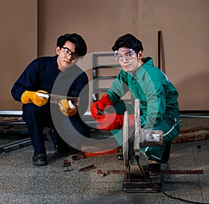 Two smart Asian engineers wearing a mechanic jumpsuit, safety glasses, and glove sitting and holding tools posing smiling to a