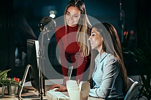 Two smart business women working together with laptop while talking in the office at night