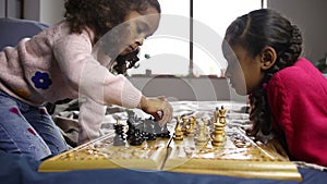 Two smart little girls playing chess on bed