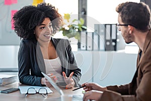 Two smart multiethnic business people working together with laptop while talking about job news in the office