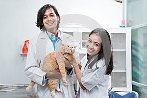 two smiling asian vets looking at the camera while checking brown cat