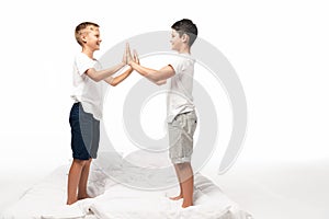 Two smiling brothers clapping hands while standing on bed