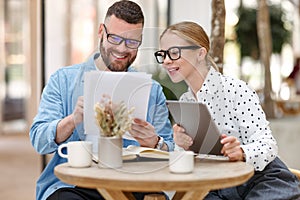 Two smiling business colleagues young man and woman working together on project at outdoor cafe