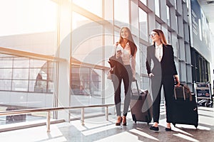 Two smiling business partners going on business trip carrying suitcases while walking through airport passageway