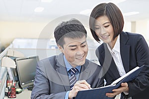 Two Smiling Business People Looking Down at Note Pad and Working Together