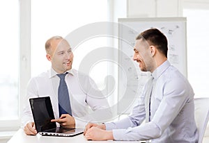 Two smiling businessmen with laptop in office