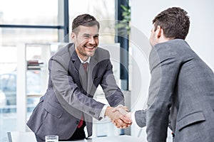 Two smiling businessmen shaking hands at meeting in office