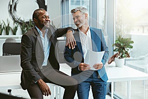 Two smiling businessmen talking about deal sitting in meeting room in modern office