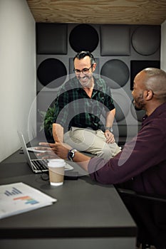 Two smiling businessmen working on a laptop in an office cubicle