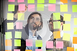 Two smiling businessmen writing tasks on sticky papers, post it