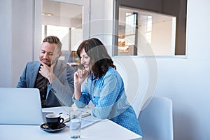 Two smiling businesspeople working on a laptop in an office