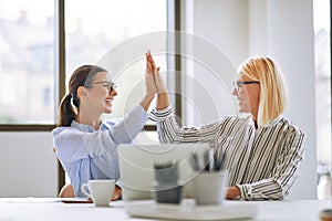 Two smiling businesswomen high fiving together in an office photo