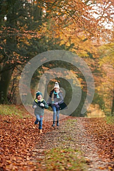 Two Smiling Children Having Fun Running Along Path Through Autumn Woodland Together