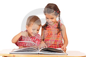 Two smiling children reading the book on the desk