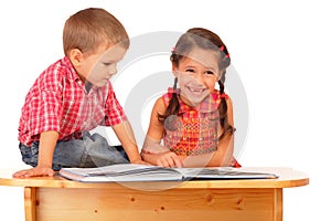 Two smiling children reading the book on the desk