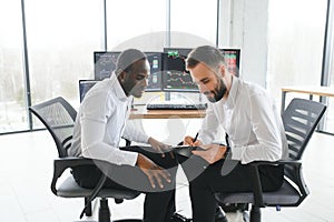 Two smiling confident businessmen, financial analysts or investment advisers sitting at office desk