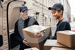 Two smiling couriers unloading cardboard boxes from van in the city
