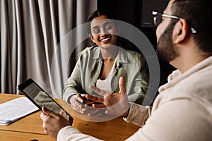 Two smiling coworkers discussing business details and working on tablet while sitting in office