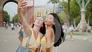 Two smiling diverse female friends looking at smartphone screen and making selfie portrait