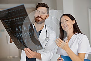 Two of smiling doctors in uniform look and discuss an X Ray or MRI scan of the patient spine