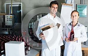 Two smiling employees standing in packaging section on wine manufactory