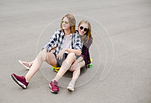 Two smiling female friends having fun riding yellow longboard on the street. Friendship concept