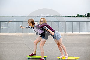 Two smiling female friends learning riding longboard with helping each other. Friendship concept