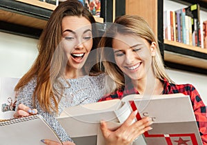 Two smiling female students reading books at the library