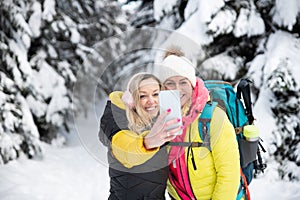 Two smiling friends take a picture of themselves in the mountains on a winter trail.