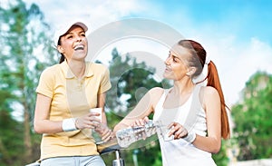 Two smiling girl friends in sports clothing drinking water