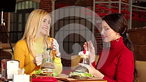Two smiling girls drink cocktails and eat burgers in a bright restaurant