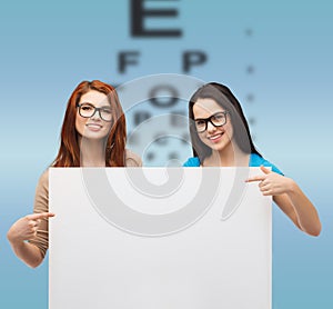 Two smiling girls with eyeglasses and blank board