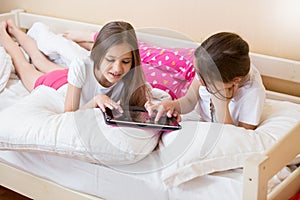 Two smiling girls lying in bed and using digital tablet