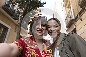 Two smiling girls taking a photo together with mobile phone outdoors