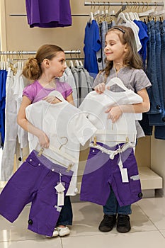 Two smiling girls trying on the same dress in the store