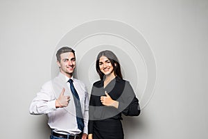 Two smiling happy businesspeople in formalwear showing thumbs-up on gray