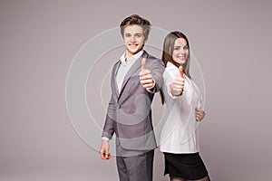 Two smiling happy business people in formalwear showing thumbs-up on gray background