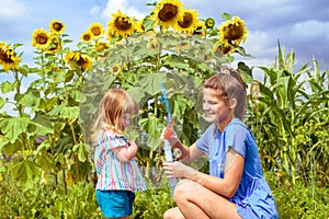 Two smiling happy children in sunflowers field laugh and blow bubbles. summer in the village