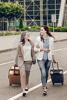 Two smiling happy friends with suitcases near the airport. Women co-workers returning from a joint business trip