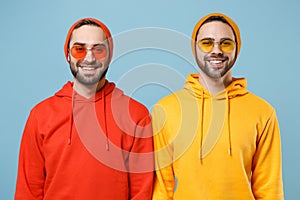 Two smiling hipster men guys in fashion red yellow clothes eyeglasses posing isolated on pastel blue background studio