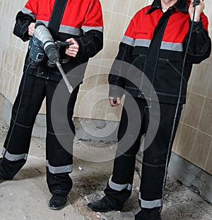 Two smiling house-builders in uniform holding construction tools